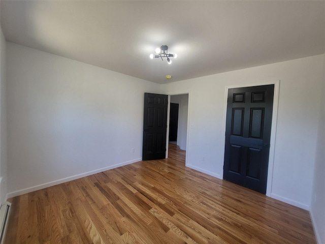 unfurnished bedroom featuring baseboard heating, baseboards, and wood finished floors