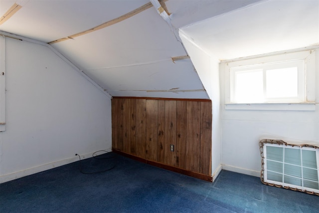 additional living space featuring baseboards, carpet, wood walls, and vaulted ceiling