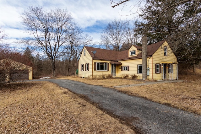 cape cod house with roof with shingles, a chimney, and driveway