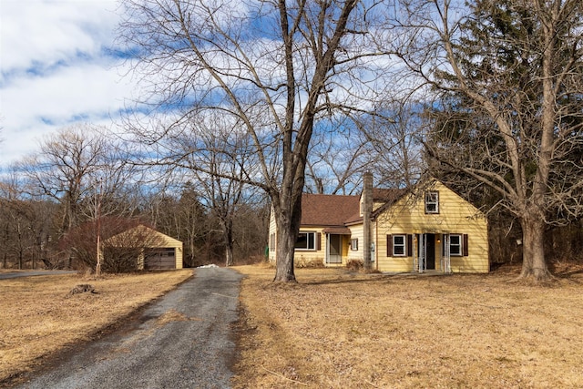 view of front facade featuring a detached garage, an outbuilding, roof with shingles, and a chimney