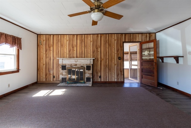 unfurnished living room with a glass covered fireplace, wooden walls, a wealth of natural light, and ornamental molding