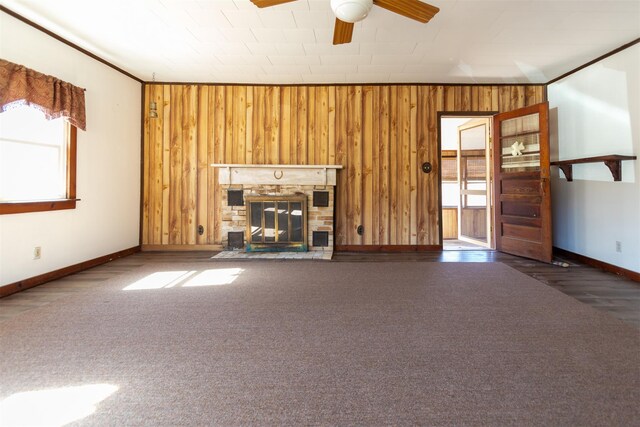 unfurnished living room featuring ornamental molding, a ceiling fan, a glass covered fireplace, carpet floors, and wooden walls