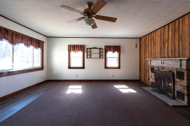 unfurnished living room with a ceiling fan, baseboards, a fireplace, ornamental molding, and wood walls