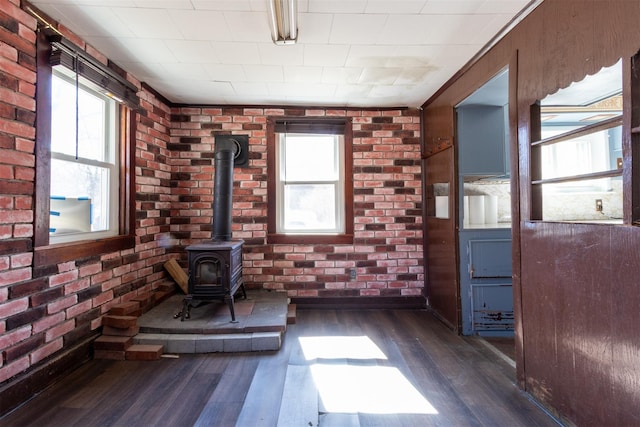 interior space with brick wall, a wood stove, and dark wood-type flooring