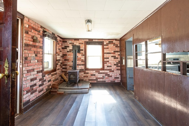 unfurnished living room featuring dark wood finished floors, a wood stove, a healthy amount of sunlight, and brick wall