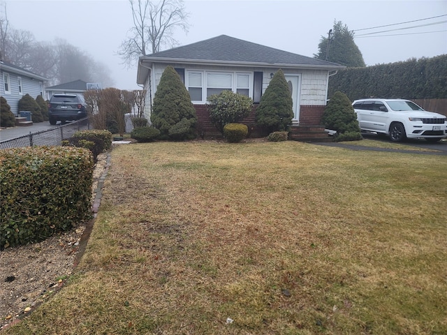 bungalow-style home featuring brick siding, roof with shingles, fence, and a front yard