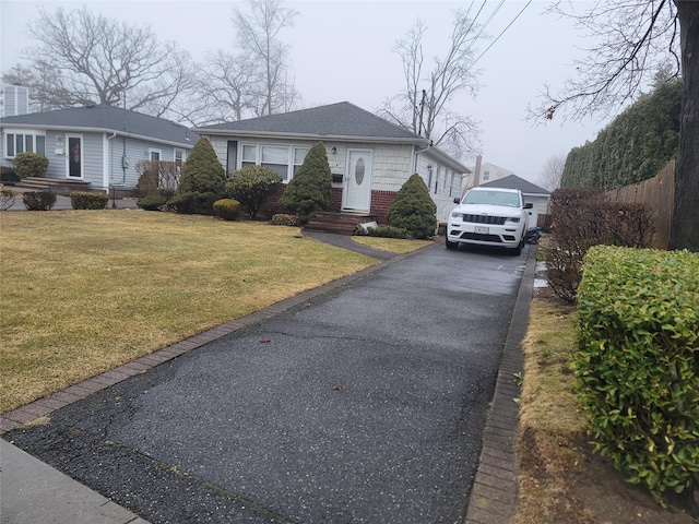 bungalow-style home featuring driveway, brick siding, a front lawn, and a shingled roof