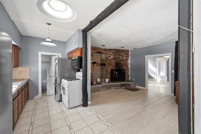 kitchen featuring tasteful backsplash, stainless steel microwave, brown cabinetry, a brick fireplace, and white gas range oven