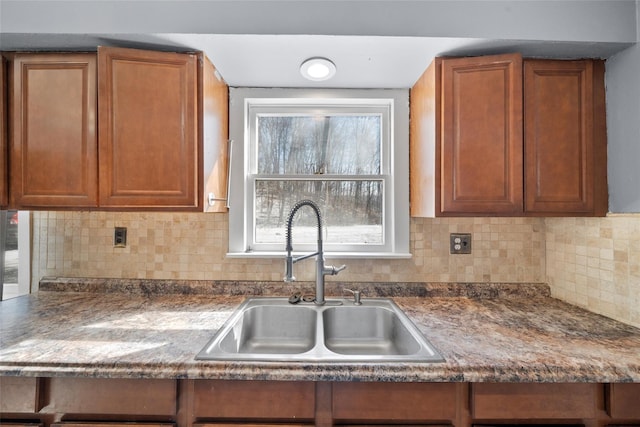 kitchen featuring dark countertops, backsplash, brown cabinets, and a sink