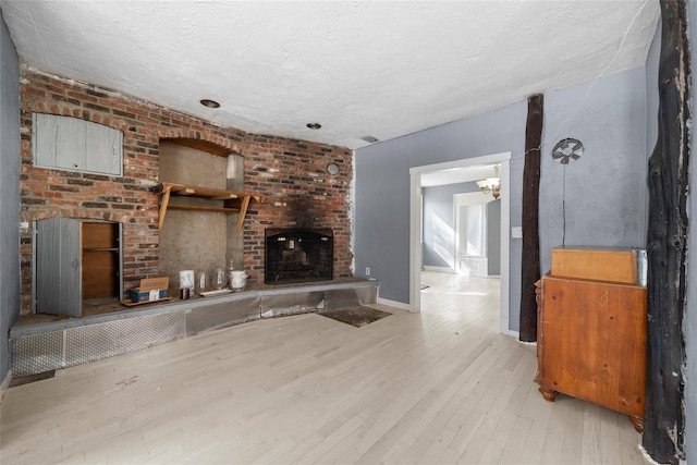 living room featuring light wood-style floors, a brick fireplace, baseboards, and a textured ceiling