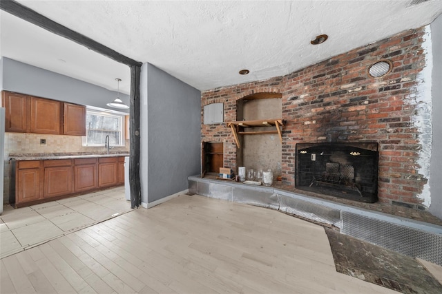 unfurnished living room with light wood-style floors, a brick fireplace, a sink, a textured ceiling, and baseboards