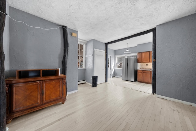 unfurnished living room with light wood-type flooring, a textured wall, baseboards, and a baseboard radiator