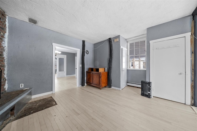 unfurnished living room featuring a textured ceiling, a textured wall, a baseboard radiator, visible vents, and light wood-type flooring