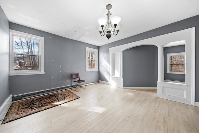 unfurnished room with arched walkways, a notable chandelier, baseboards, light wood-style floors, and baseboard heating