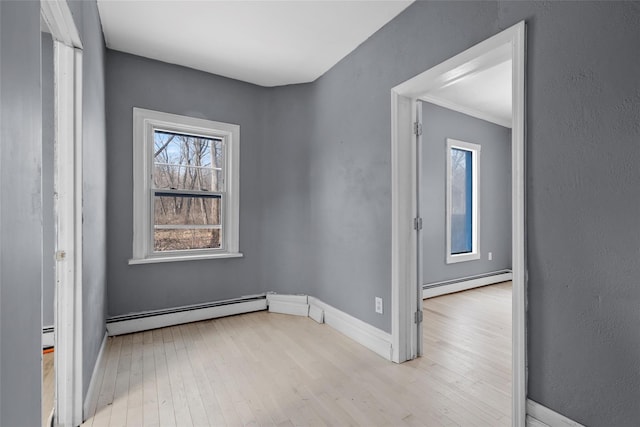 empty room with a baseboard radiator, baseboards, and light wood finished floors