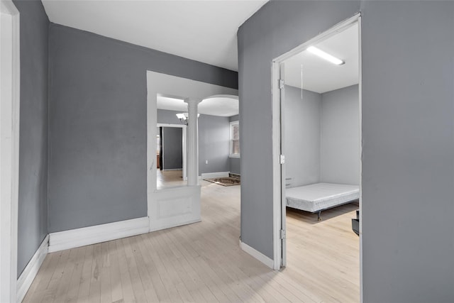 unfurnished room featuring light wood-style floors, baseboards, arched walkways, and ornate columns