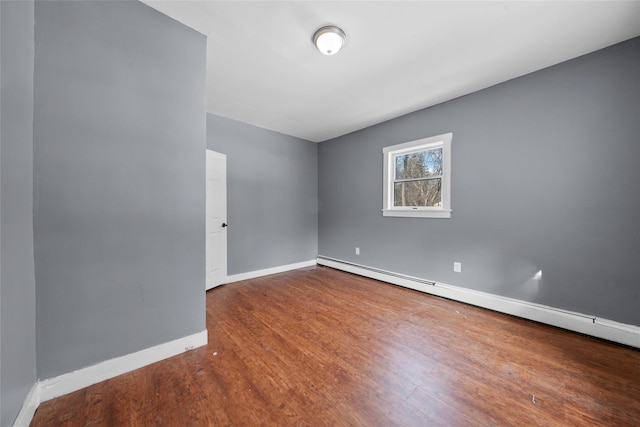 unfurnished room with baseboard heating, wood finished floors, and baseboards