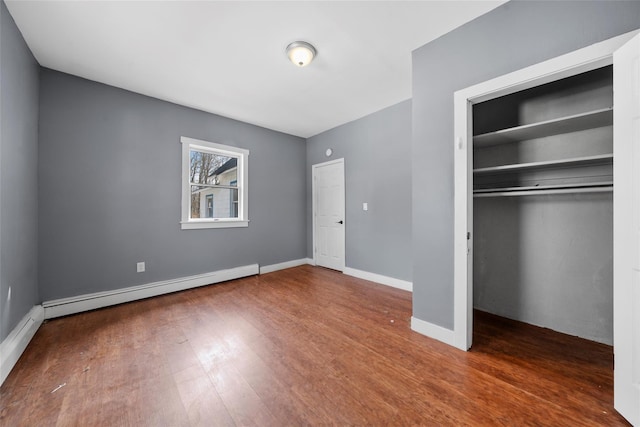 unfurnished bedroom with a closet, baseboards, baseboard heating, and wood finished floors