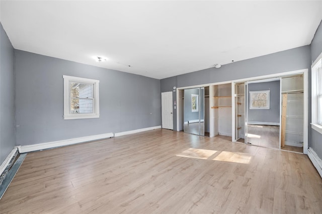 empty room featuring a baseboard heating unit, light wood-type flooring, and baseboards