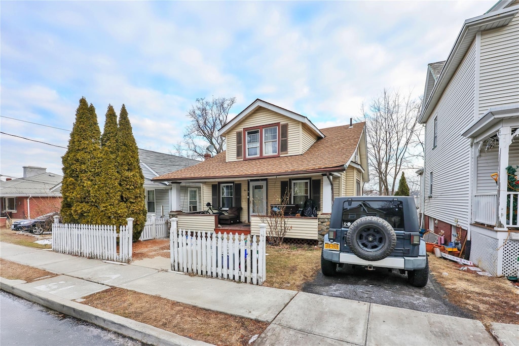 view of front of house featuring driveway, a porch, a fenced front yard, and a shingled roof