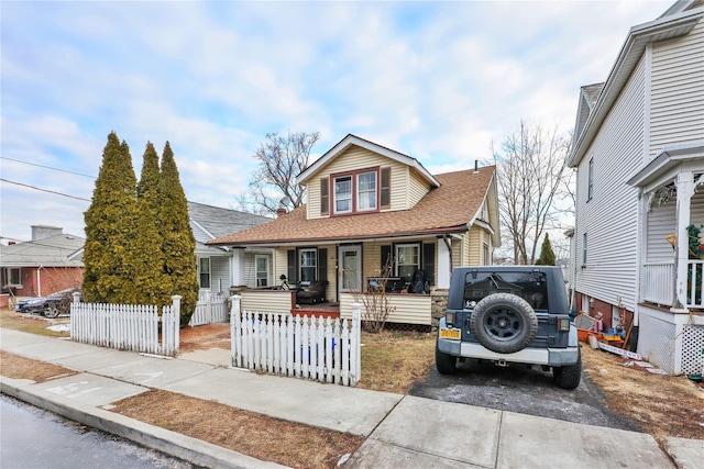 view of front of house featuring driveway, a porch, a fenced front yard, and a shingled roof