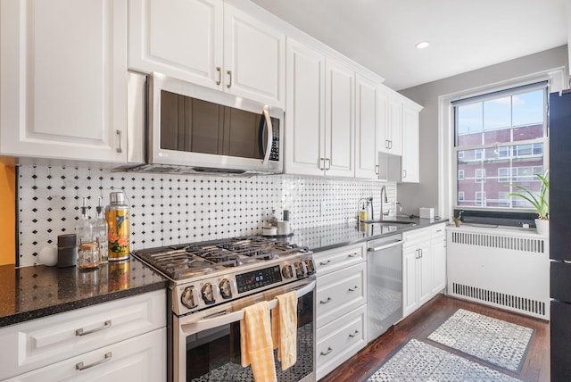 kitchen featuring a sink, white cabinets, appliances with stainless steel finishes, dark stone counters, and radiator heating unit