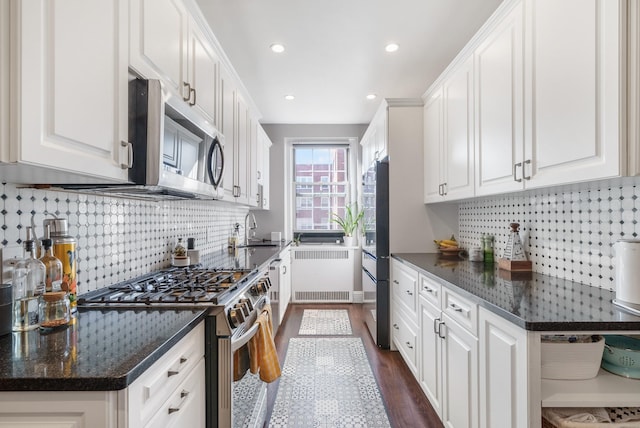 kitchen featuring stainless steel appliances, a sink, white cabinets, radiator, and dark stone counters