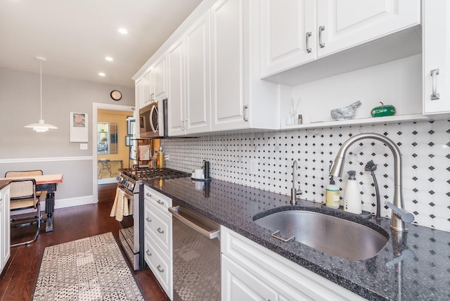 kitchen with pendant lighting, appliances with stainless steel finishes, white cabinets, a sink, and dark stone counters