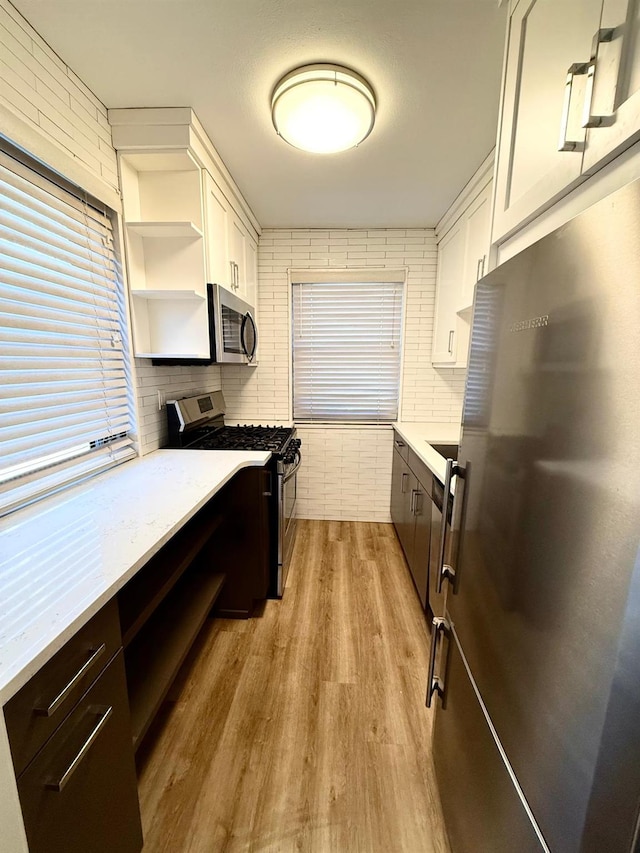 kitchen with white cabinets, light wood-style flooring, appliances with stainless steel finishes, light countertops, and open shelves