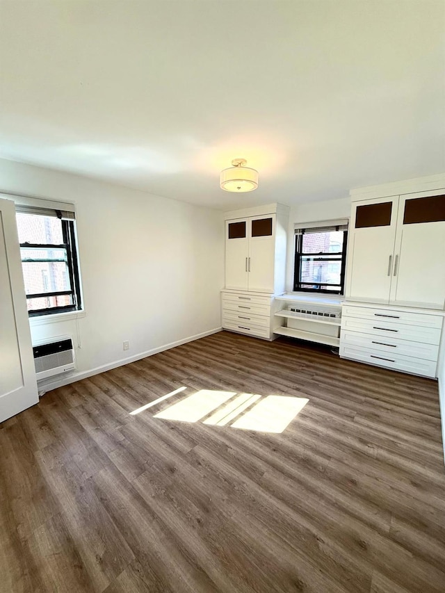 unfurnished bedroom featuring an AC wall unit, multiple windows, dark wood finished floors, and baseboards