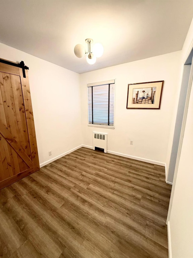 unfurnished bedroom featuring dark wood-style floors, a barn door, baseboards, and radiator