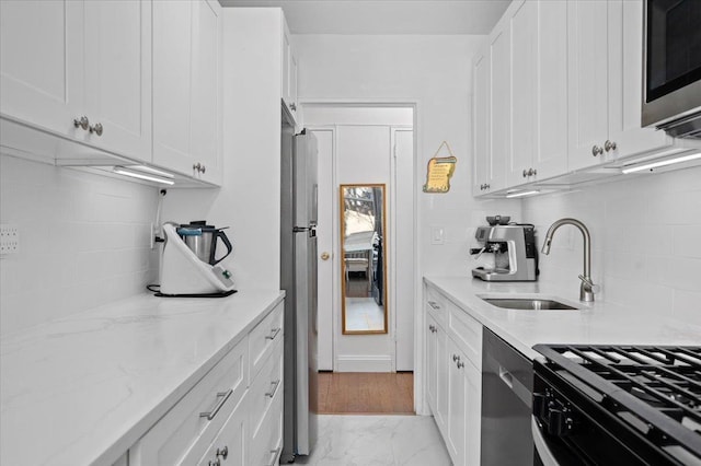 kitchen with marble finish floor, stainless steel appliances, white cabinetry, a sink, and light stone countertops