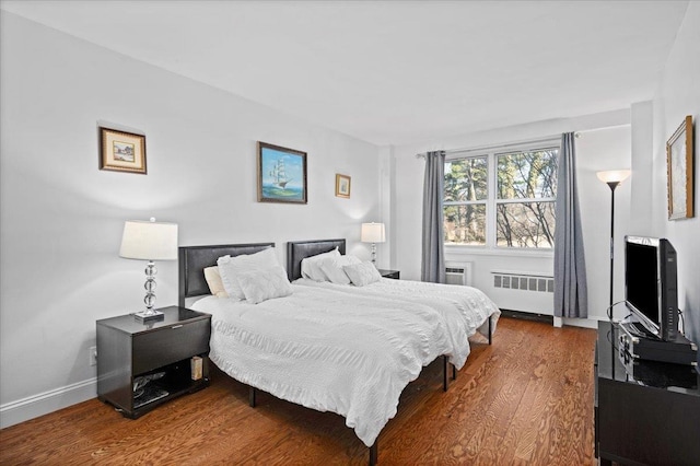 bedroom with radiator heating unit, baseboards, and wood finished floors