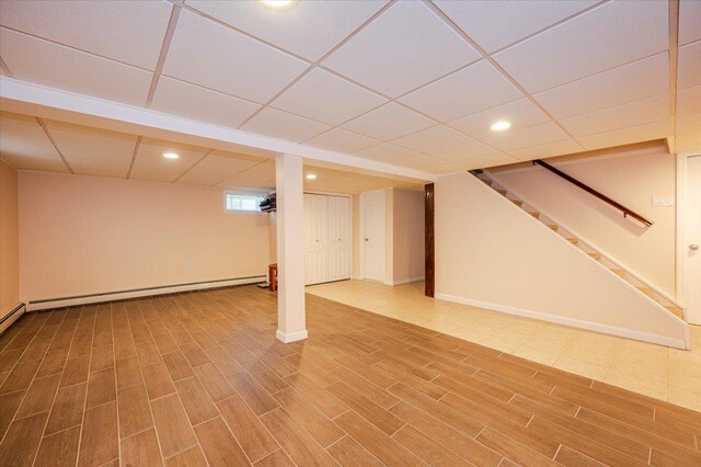 below grade area with recessed lighting, wood finished floors, stairs, baseboards, and a paneled ceiling