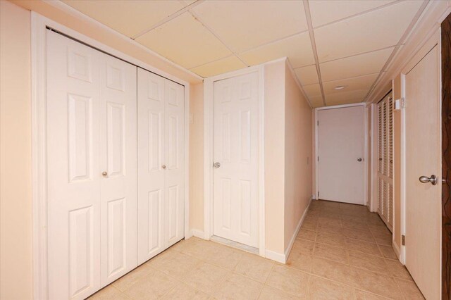 hallway featuring light tile patterned flooring, a paneled ceiling, and baseboards