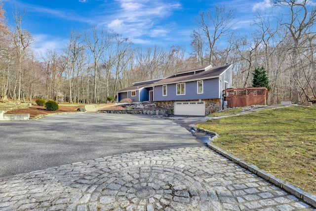 view of front facade with aphalt driveway, a wooden deck, a garage, stone siding, and a front lawn