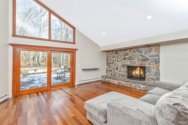 living area with high vaulted ceiling, a baseboard radiator, a stone fireplace, and wood finished floors