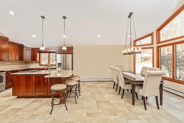 kitchen with stainless steel appliances, decorative light fixtures, a center island with sink, and light stone counters