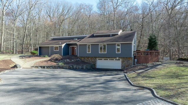 view of front of home with an attached garage, a view of trees, stone siding, and driveway