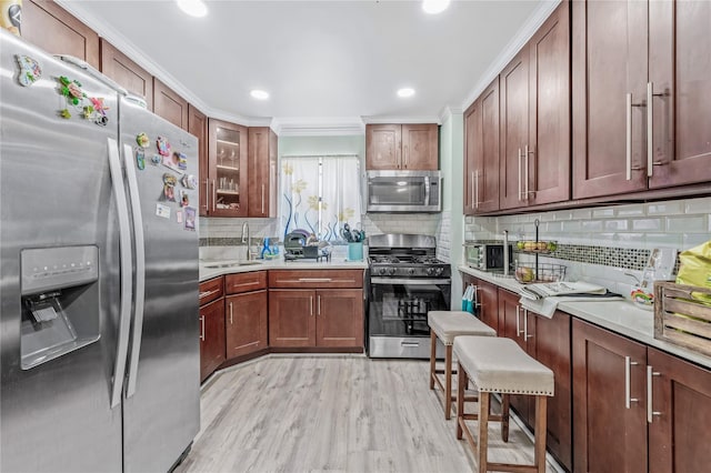 kitchen with a breakfast bar area, a sink, light countertops, appliances with stainless steel finishes, and glass insert cabinets