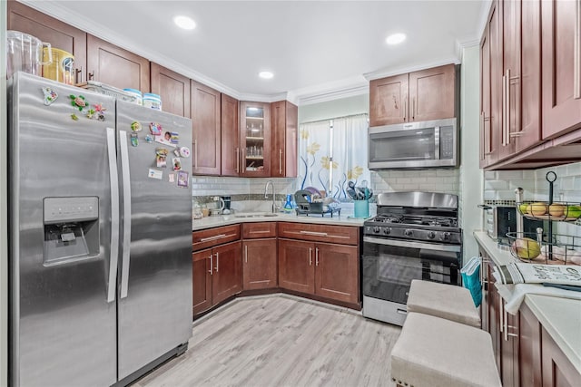 kitchen with stainless steel appliances, light countertops, light wood-style flooring, glass insert cabinets, and a sink