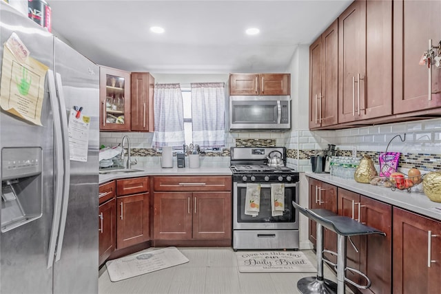 kitchen with stainless steel appliances, light countertops, backsplash, glass insert cabinets, and a sink