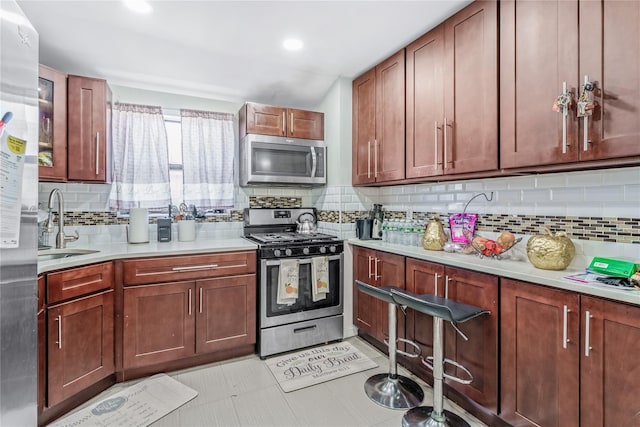 kitchen featuring stainless steel appliances, light countertops, decorative backsplash, light tile patterned flooring, and a sink