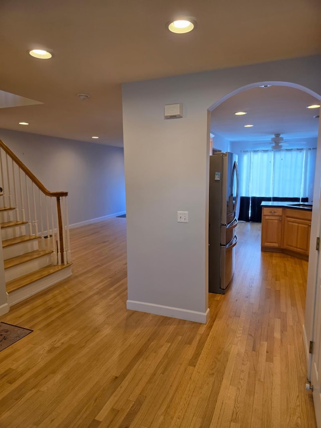 hallway featuring arched walkways, stairway, a sink, and light wood-style floors