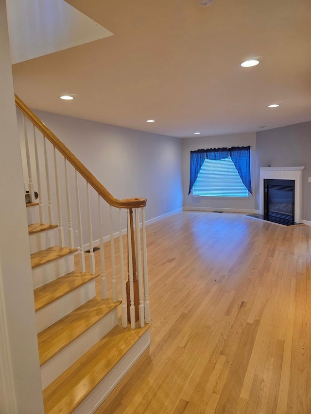 unfurnished living room with baseboards, stairway, wood finished floors, and recessed lighting