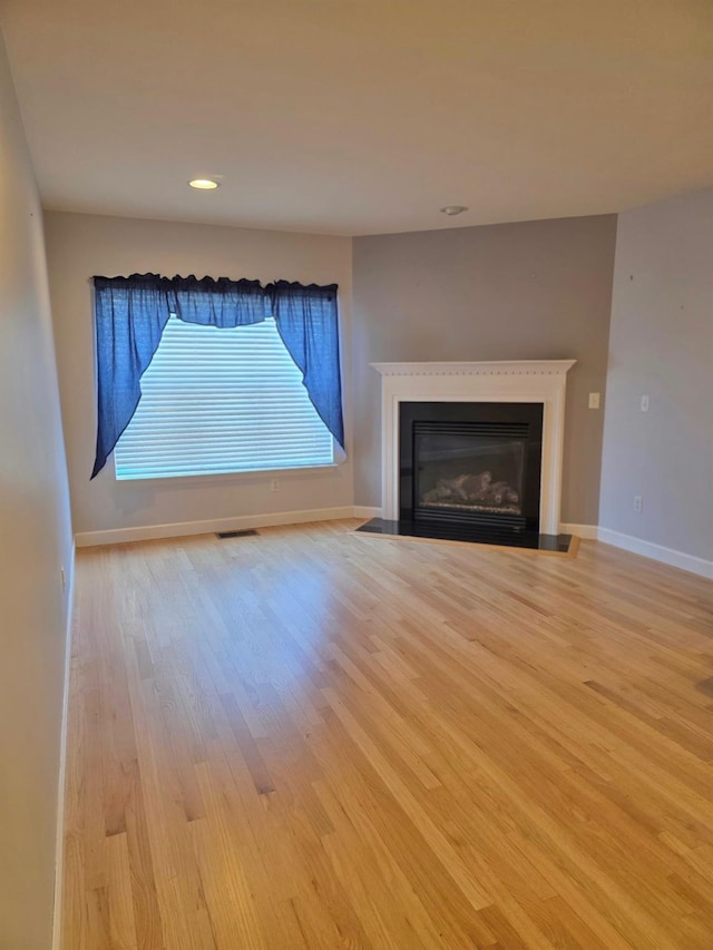 unfurnished living room featuring recessed lighting, visible vents, a fireplace with flush hearth, wood finished floors, and baseboards