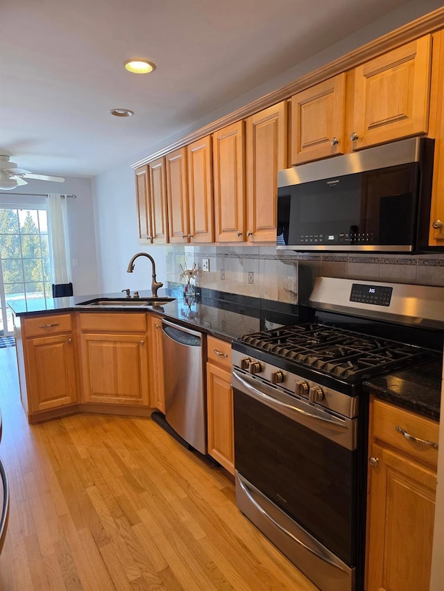 kitchen featuring light wood finished floors, decorative backsplash, a peninsula, stainless steel appliances, and a sink