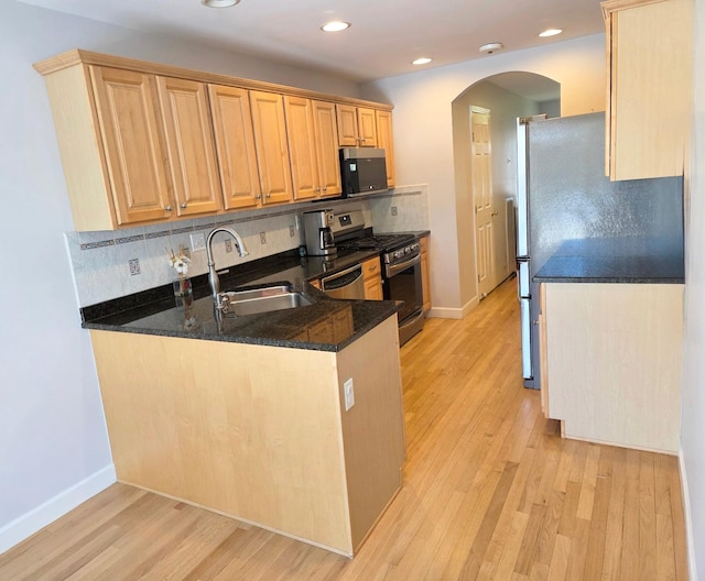 kitchen featuring arched walkways, tasteful backsplash, appliances with stainless steel finishes, light wood-style floors, and a sink