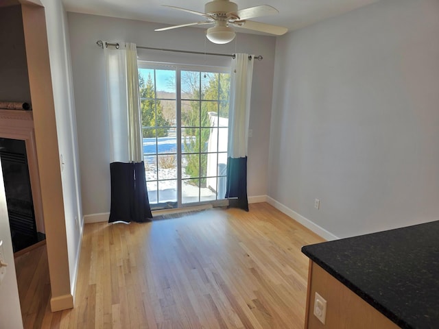 interior space featuring light wood-style flooring, baseboards, a ceiling fan, and a glass covered fireplace