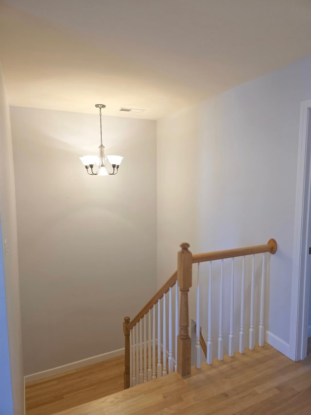 stairway with baseboards, wood finished floors, and a notable chandelier